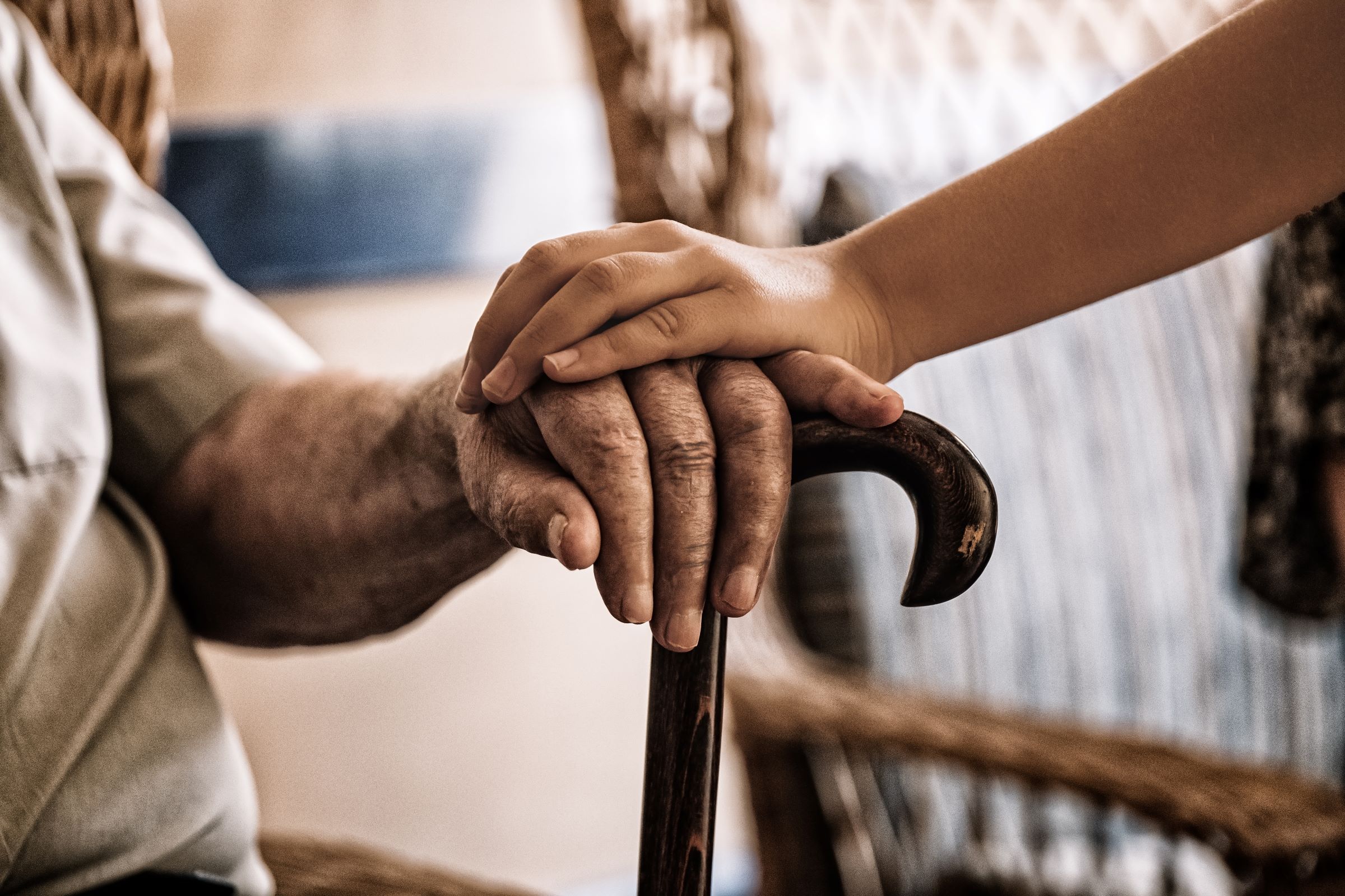 Young person clasps the hand of senior family member who uses cane.